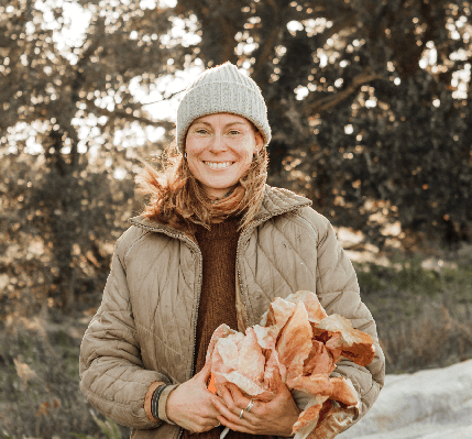 Calixta of local grower; Flourish Farm stands holding produce whilst smiling at the camera
