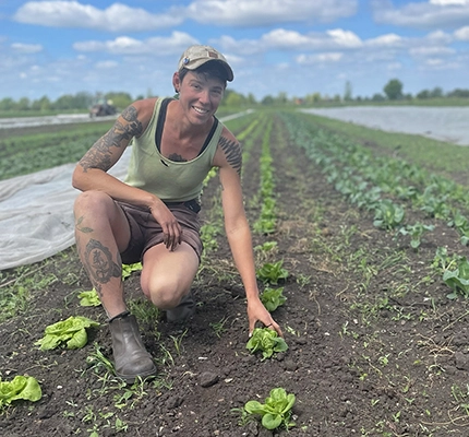 Organic Farmer, Heron, smiles to the camera while kneeling in a fenland field growing lettuces