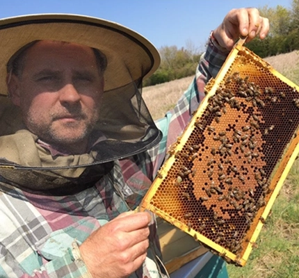 Peter holds up a honeycomb to the camera while wearing a beekeepers protective headgear