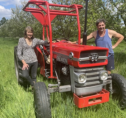 Doreen and Paul of local grower Waterland Organics stand next to a red tractor whilst in their orchard